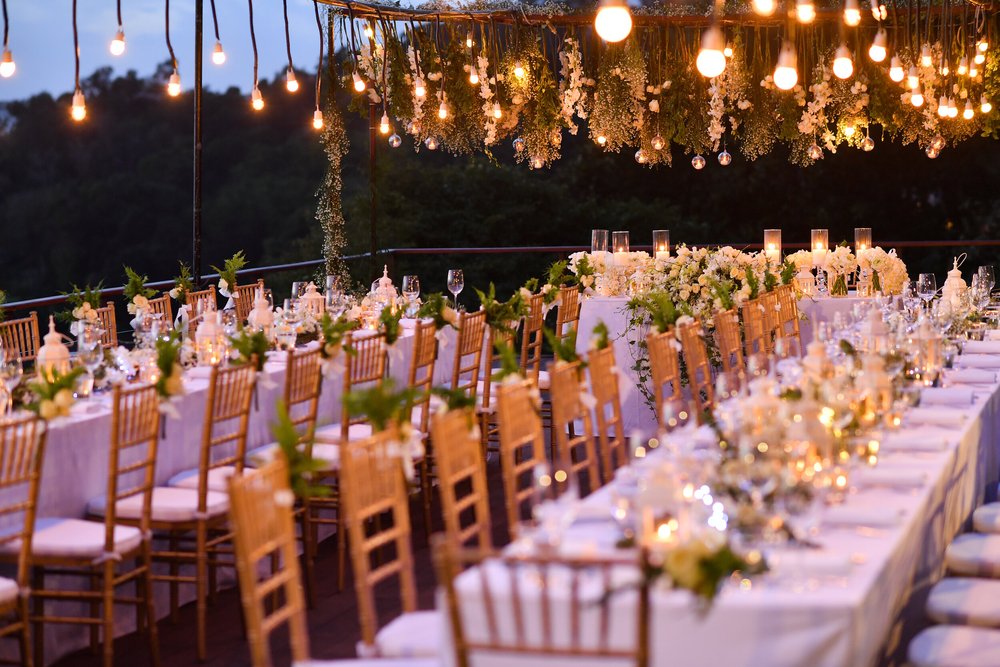 A long event table beneath Edison bulbs and greenery